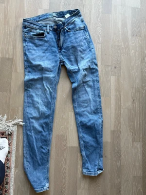 Två par slim fit jeans herr - Säljer två par slim fit jeans i herrmodell, ett par i ljusblå tvätt med slitningar och ett par i svart. Båda har klassisk femficksdesign och dragkedjegylf. Perfekta för en avslappnad och trendig stil. Materialet är bomullsdenim med lite stretch för extra komfort.