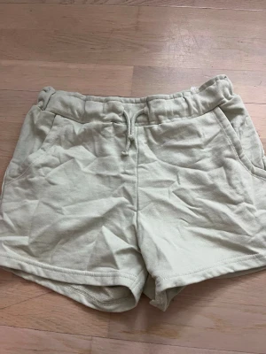 Ljusgröna mjukisshorts med snörning - Säljer ett par ljusgröna mjukisshorts med snörning i midjan och två sidofickor. Shortsen har en relaxed passform och är perfekta för varma dagar eller chill hemma. Tillverkade i mjukt bomullstyg för extra komfort. De är lite skrynkliga pga att jag inte har strukit dem