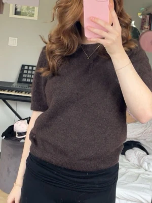 Brun kortärmad stickad tröja - Mysig brun stickad tröja med korta ärmar och rund hals. Tröjan har en enkel, klassisk design och är perfekt för lager på lager. Materialet ser mjukt och bekvämt ut, och den ribbade kanten ger en snygg finish.