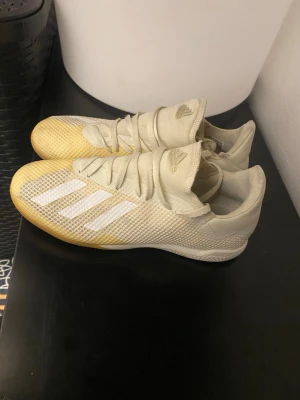 Vita Adidas fotbollsskor med mesh - Säljer ett par vita Adidas fotbollsskor med klassiska tre ränder på sidan. Skorna har en låg profil, snörning och ovandel i meshmaterial för bra ventilation. Adidas-logga på plösen och sidorna. Perfekta för dig som vill ha lätta och snygga skor på planen.