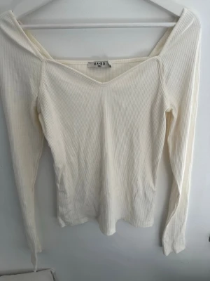 Vit ribbad topp från NAKD - Säljer en vit ribbad topp från NAKD med v-ringad hals och långa ärmar. Toppen har en slim passform perfekt för att styla med jeans eller kjol.