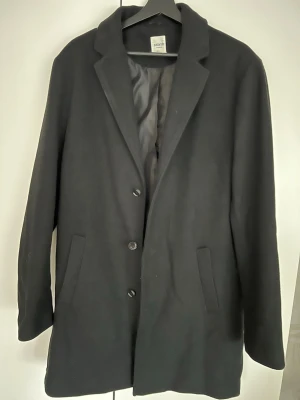 Svart klassisk rock - Stilren svart rock köpt på Zalando med tre knappar framtill och två snedställda fickor. Klassisk krage och helfodrad insida ger en clean look. Perfekt för dig som vill ha en enkel men snygg rock till hösten eller vintern. Strl L