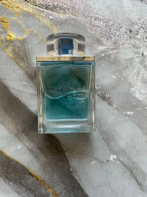 Baldessarini Nautic Spirit parfym - Fräsch parfym från Baldessarini, Nautic Spirit, i en stilren fyrkantig glasflaska med blått innehåll och silverfärgat lock. Flaskan har en modern design med kompassdetalj på baksidan och genomskinliga kanter. Perfekt för dig som gillar marina dofter.