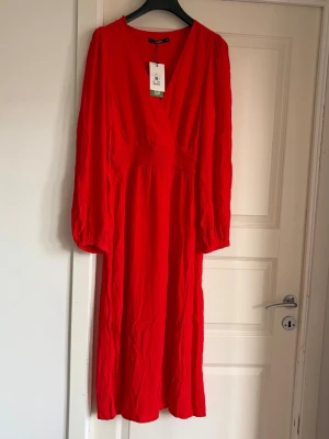Röd omlottklänning från Cubus - Snygg röd omlottklänning från cubus i storlek M  med v-ringning och långa ärmar. Klänningen har en markerad midja och ett luftigt fall som ger en avslappnad men ändå chic look. Perfekt för dig som vill sticka ut med färg och stil. Storlek 