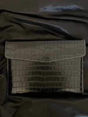 Datorfodral med krokodil mönster  - Stilrent datorfodral tillverkat av veganskt läder i vattentätt material. Fodralet stängs med knapp. Fodralet skyddar din dator effektivt samtidigt som det ger din outfit en extra touch. ⚜️ Storlek: 34 × 25 cm –  Innifrån 33 x 24 📦  