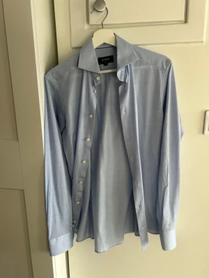 Ljusblå skjorta från Eton slim fit - Snygg ljusblå skjorta från Eton i slim fit-modell. Skjortan har klassisk krage, vita knappar och långa ärmar med breda manschetter. Tillverkad i mjuk bomull som känns skön mot huden. Perfekt för en clean och stilren look.