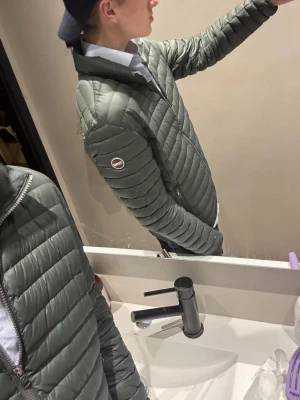 Colmar jacka - Snygg grön pufferjacka från colmar med quiltad design och hög krage. Jackan har dragkedja framtill och colmar på ärmen. Perfekt för kalla dagar och riktigt lätt att bära. Size 50