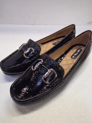 Brand New Hush Puppies Leather Loafers stl 40-24.5cm ordinary price 799kr  - ​Elegant Hush Puppies Black Patent Leather Loafers ​Elevate your footwear collection with these timeless and sophisticated loafers from Hush Puppies. Known for their perfect blend of style and comfort, these shoes are ideal for professional wear, formal events, or adding a touch of class to a casual outfit. ​Key Features: ​Premium Material: High-shine black patent leather with a subtle textured finish. ​Stylish Accents: Featuring a classic silver-toned bit detail (buckle) across the vamp for a p