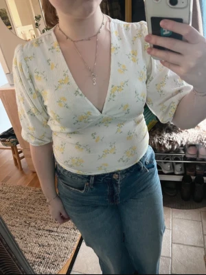 Vit blommig blus med v-ringning - Söt vit blus med gula blommor och djup v-ringning. Knappt använd! 