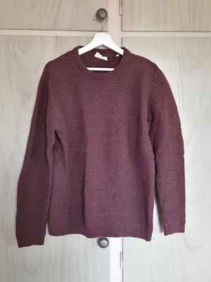 Stickad tröja i vinrött zigzagmönster - Mysig vinröd stickad tröja med diskret zigzagmönster. Tröjan har rund halsringning, långa ärmar och ribbade muddar vid ärmslut och nederkant. Perfekt för kyliga dagar och enkel att matcha med ett par jeans.                                                     Alla kläder rollas innan dom skickas hem då det finns katt i hemmet🐈 Jag stryker och tvättar INTE innan jag skickar det får du stå för själv så det blir som du vill ha det🤗