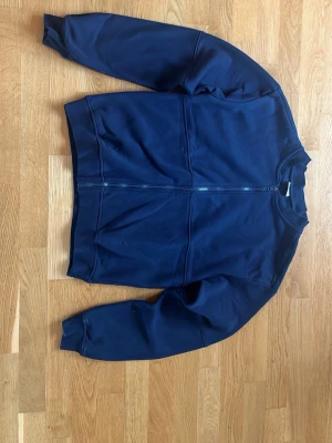 Mörkblå zip hoodie - En enkel och stilren mörkblå hoodie med dragkedja framtill och två fickor. Hoodien har långa ärmar och ribbade muddar vid ärmslut och nederkant. Perfekt för en avslappnad look och passar till det mesta. Materialet känns mjukt och bekvämt.