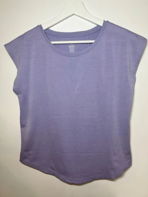 Ljuslila topp från SOC - En enkel och stilren ljuslila topp från SOC med rund halsringning och korta ärmar. Tillverkad i ett mjukt och lätt material som passar perfekt till träning eller avslappnade dagar. Modellen har en rak passform och diskret logga nere vid fållen.