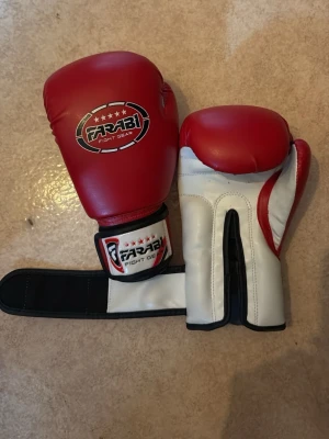 Röda boxningshandskar Farabi - Säljer ett par röda och vita boxningshandskar från Farabi Fight Gear. Handskarna har kardborreknäppning vid handleden och är tillverkade i syntetmaterial. Perfekta för träning inom boxning eller kampsport.