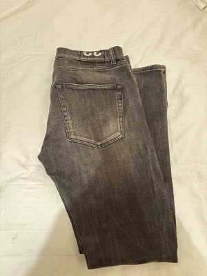 Grå tvättade jeans från Dondup - Säljer ett par grå tvättade jeans från Weekday med klassisk femficksmodell och raka ben. Jeansen har en snygg sliten look och är tillverkade i mjuk denim med lite stretch för extra komfort. Perfekta för en avslappnad och trendig stil.