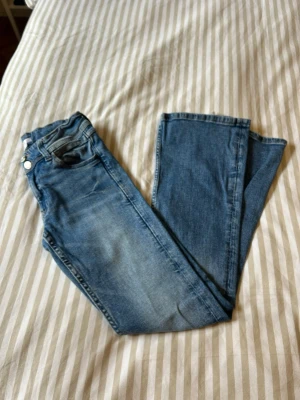 Blå bootcut jeans från Gina Tricot  - Säljer ett par blå bootcut jeans som är sköna att ha på sig.  Jeansen har normal midja som man kan spänna in och ut och dragkedja med knapp. Materialet är mjukt denim i bomull. 