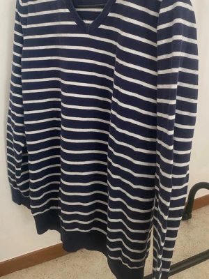 Randig marinblå tröja med V-ringning - Snygg marinblå tröja med vita horisontella ränder och V-ringad hals. Tröjan har långa ärmar och ribbade muddar vid ärmslut och nederkant. Perfekt för dig som gillar klassisk och avslappnad stil.