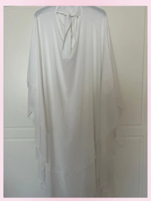 Vit lång khimar - 💗Elegant vit khimar med lös passform och knyt. har ett flytande fall och flera lager tyg som ger en mjuk volang-effekt längs sidorna. Perfekt för dig som gillar minimalistisk och stilren design.💞