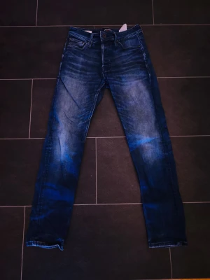 Blå jeans från Jack & Jones - Säljer ett par snygga blå jeans från Jack & Jones med klassisk tvätt och raka ben. Jeansen har en cool slitningseffekt och är tillverkade i bomull med lite stretch för extra komfort. Perfekta till vardagslooken!
