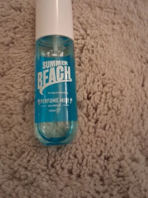 Summer Beach Perfume Mist 100ml - Fräsch parfymmist med doft av havsbris från Summer Beach. Flaskan är genomskinlig med blå vätska och vitt lock. Passar både hår och kropp. Innehåller 100 ml och har en modern, enkel design som ger sommarkänsla.