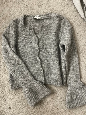 Grå stickad kofta från AWARE XS - Mysig grå stickad kofta från AWARE i storlek XS. Koftan har rund halsringning, pärlknappar framtill och långa ärmar med breda ribbade muddar. Perfekt för lager på lager och ger en chill vibe till din outfit. Andvänd endast 1 gång
