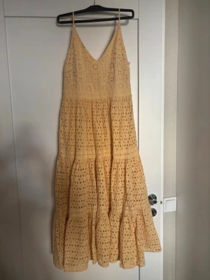 Ljusgul långklänning med spetsdetaljer - Söt långklänning i ljusgul ton med tunna axelband och v-ringning. Klänningen har broderade spetsdetaljer och volanger, samt ett mjukt innerfoder. Perfekt för varma dagar och somriga tillfällen.