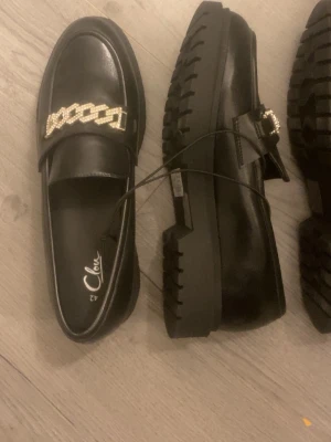 Svarta loafers med kedjedetalj - Ett par eleganta skor med liten klack, passar till vardags och fest, storlek 42, aldrig använda, original pris är 450kr säljer dem för 200 vid snabbt köp 
