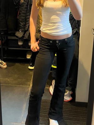 Svarta bootcut jeans - Säljer ett par svarta bootcut jeans med hög midja och utsvängda ben. Jeansen har klassisk femficksdesign och stängs med knapp och dragkedja. Perfekta för en trendig och avslappnad look.