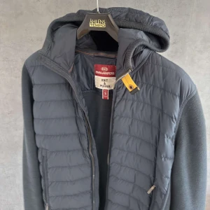  Parajumpers jacka  - Snygg mörkblå pufferjacka från Parajumpers med stickade ärmar och huva. Jackan har dragkedja framtill, två sidofickor med dragkedja och den klassiska gula detaljen vid halsen. Perfekt för kyliga dagar och riktigt skön att bära. Jackan är välvårdad och i riktigt bra skick nypris runt 7000kr 