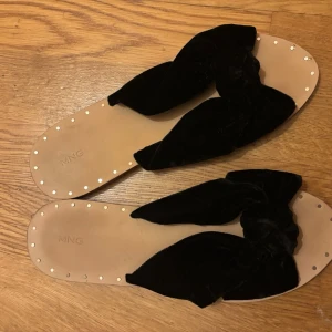 Beiga sandaler med svart rosett i sammet - Snygga sandaler från Mango med breda svarta sammetsband och stor rosett på ovansidan. Sulan är rejäl och har små guldfärgade nitar längs kanten vilket får skon att se lyxig ut. Använda max någon gång.