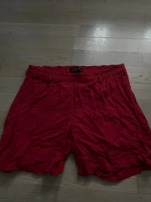 Röda shorts från Marine - Säljer ett par röda shorts från Marine med elastisk midja. De har en enkel och avslappnad passform, perfekta för varma dagar. Materialet känns lätt och luftigt, vilket gör dem sköna att bära under sommaren.