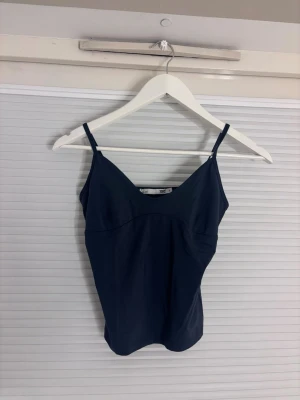 Mörkblå linnetopp med smala band - En enkel och stilren mörkblå linnetopp med smala axelband och v-ringad hals. Perfekt att matcha med jeans eller kjol för en clean look. Materialet känns mjukt och följsamt mot huden.