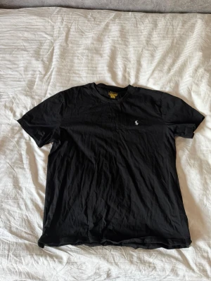 Svart t-shirt från Polo  Ralph Lauren - Klassisk svart t-shirt från Ralph Lauren med den ikoniska loggan broderad på bröstet. T-shirten har rund halsringning och korta ärmar. Tillverkad i mjuk bomull som känns skön mot huden. Perfekt basplagg till garderoben. Pris kan diskuteras vid snabb affär.
