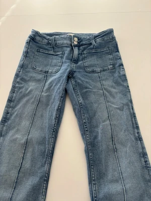 Low waist bootcut jeans från Gina Young - Säljer ett par blå jeans från Gina Tricot med  markerade sömmar framtill. Jeansen har två stora fickor fram samt två fickor där bak. Mycket bra skick och sparsamt använda. Har en liten liten rosa fläck/prick där fram som knappt syns (Bild finns) 