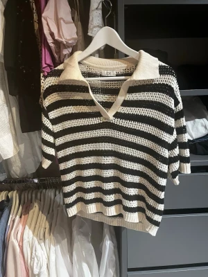 Randig stickad tröja från JDY - Säljer en svartvit stickad tröja från JDY med breda horisontella ränder och öppen stickning. Tröjan har krage, v-ringning och halvlånga ärmar. Perfekt för en avslappnad och trendig look.