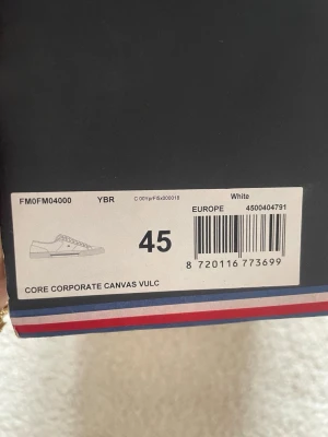 Vita Tommy Hilfiger canvas sneakers - Snygga vita sneakers från Tommy Hilfiger i canvasmaterial. Klassisk låg modell med vita snören och diskreta detaljer i rött och blått. Perfekta för dig som gillar stilrena och tidlösa skor med en sportig touch.