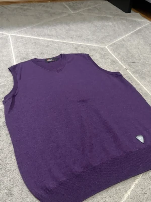 Lila stickad väst från Mango - Lila stickad väst från Mango med V-ringning och ribbade kanter. Västen har en liten metallbadge med Mango-logga nedtill och är gjord i mjukt material för en clean look.