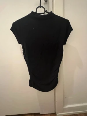 Svart topp med snatched sidor - Svart kortärmad topp som är sydd för att hålla dig runt midjan. Perfekt skick använt ett par få gånger! (Säljer även på vinted)