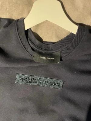 Mörkblå sweatshirt Peak Performance - Snygg mörkblå sweatshirt från Peak Performance med broderad logga på bröstet. Tröjan har rund halsringning, långa ärmar och är gjord i mjukt bomullsmaterial. Perfekt för en clean och avslappnad stil.