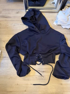 Mörkblå cropped hoodie med snörning - Snygg mörkblå cropped hoodie med huva och bred snörning i midjan. Hoodien har långa ärmar och är tillverkad i ett mjukt sweatshirtmaterial. Perfekt för en trendig och avslappnad stil.