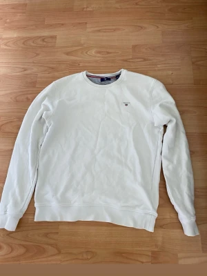 Vit sweatshirt från GANT - Klassisk vit sweatshirt från GANT med rund halsringning och broderad logga på bröstet. Tröjan har långa ärmar och ribbade muddar vid ärmslut och nederkant. Perfekt basplagg för en clean och stilren look. Går och diskuterar priset! Passar både S och M 