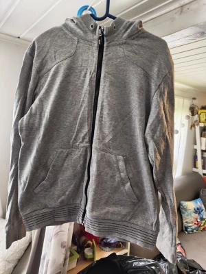 Grå hoodie från Hugo Boss/s - Snygg grå hoodie från Hugo Boss med dragkedja framtill och två stora fickor. Hoodien har ribbade muddar vid ärmslut och nederkant samt en diskret logga på bröstet. Perfekt för en avslappnad och stilren look. Saknas snöret vid huvan 