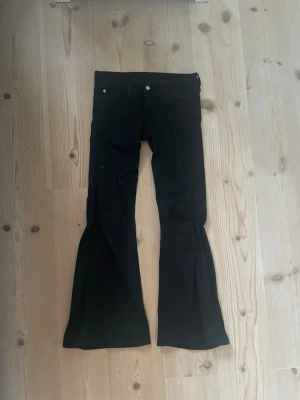 Svarta bootcut jeans med utsvängda ben från Weekday - Säljer ett par svarta bootcut jeans med utsvängda ben från weekday. Jeansen har hällor för skärp och en patch baktill i midjan. Perfekta för dig som gillar en retroinspirerad look. Jeansen är uppsydda 