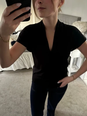Svart v-ringad topp med kort ärm - Stilren svart topp med djup v-ringning och korta ärmar. Tunn och mjuk i materialet, perfekt till jeans eller kjol. Enkel design utan mönster eller detaljer, vilket gör den lätt att matcha. Snygg och tidlös modell.
