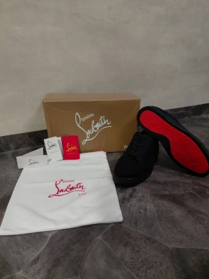 Christian Louboutin marenblå - Marenblå sneakers från Christian Louboutin med ikoniska röda sulor och diskret logga. Skorna har en klassisk låg siluett, snörning framtill och är tillverkade i ett lyxigt material. Perfekta för dig som vill sticka ut med exklusiv streetstyle.