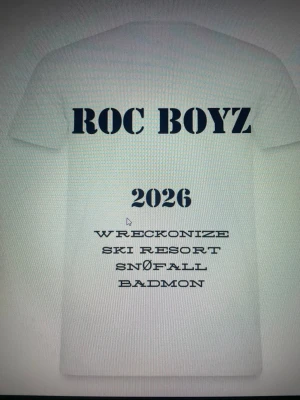Vit t-shirt ROC BOYZ 2026 - Vit t-shirt med tryck i svart text på ryggen. Stora bokstäver 'ROC BOYZ' upptill, årtalet 2026 och flera rader med text under. Klassisk passform och rund hals. Perfekt för dig som gillar streetwear och vill sticka ut.