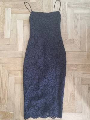 Mörkblå spetsklänning med slits från Zara - Snygg mörkblå klänning med smala axelband och blommig spets över hela plagget. Klänningen är figurnära och har en slits bak för extra rörelsefrihet. Perfekt för dig som gillar en elegant och stilren look.