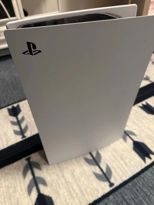 PlayStation 5 med DualSense-kontroll - Säljer en PlayStation 5 i vit och svart design från Sony. Konsolen har en futuristisk form och är tillverkad i plast. Medföljer gör en DualSense-kontroll i matchande färger, där ena spaken har ett lila grepp. Perfekt för gaming på nästa nivå.