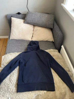 Mörkblå hoodie med dragkedja - Snygg mörkblå hoodie från Peak Performance med dragkedja framtill och huva. Modellen har två fickor och diskret logga på bröstet. Perfekt för en avslappnad stil och tillverkad i mjukt bomullsmaterial.