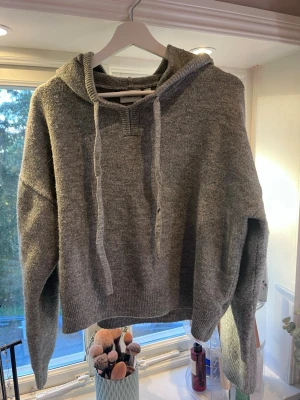 Grå hoodie från Kappahl - Mysig grå hoodie från Kappahl med huva och dragsnören. Tröjan är stickad och har ribbade muddar vid ärmslut och nederkant. Perfekt för en avslappnad och stilren look.