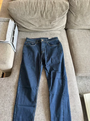 Blå slim stretchjeans från denim.co - Snygga blå slim fit jeans från denim.co med stretch för extra komfort. Klassisk femficksmodell med orangea sömmar och normal midja. Perfekta för dig som gillar en smalare passform och vill ha jeans som sitter skönt hela dagen.